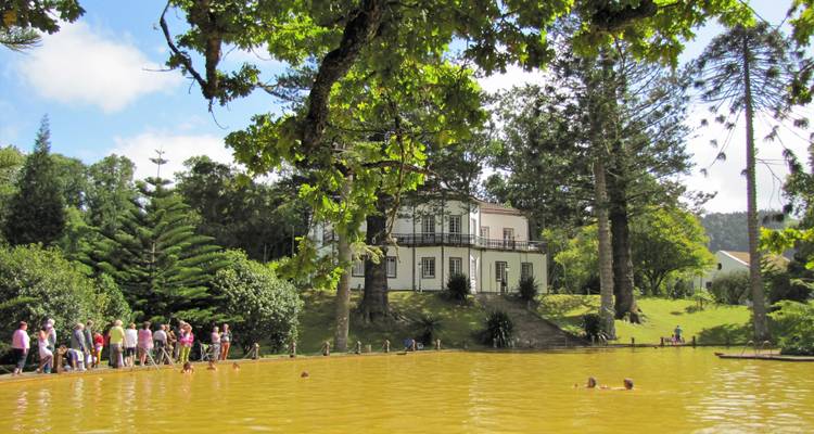 Les visiteurs se baignent dans une piscine thermale naturelle entourée d'arbres luxuriants et d'une maison de style colonial aux Açores.