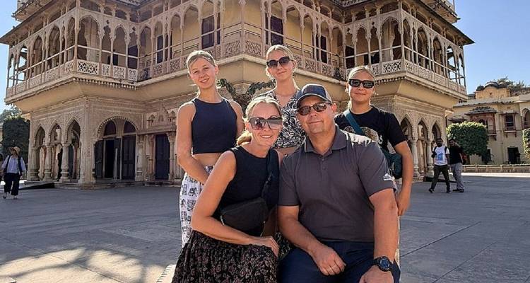 Glimlachende familie die poseert voor de sierlijke gevel van een paleis in Jaipur.