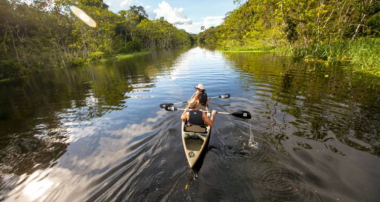 Persoon die in een kano paddelt op een rivier in een dichte jungle.