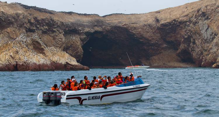 Touristen in Schwimmwesten auf einem Boot in der Nähe von felsigen Inseln.