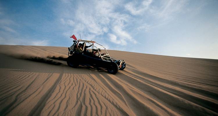 Dünenbuggy, der unter blauem Himmel eine Sanddüne hinabfährt.