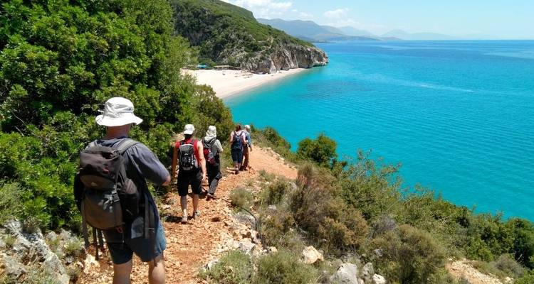 Groep wandelaars die langs een pad lopen met uitzicht op een prachtig strand met turquoise wateren.