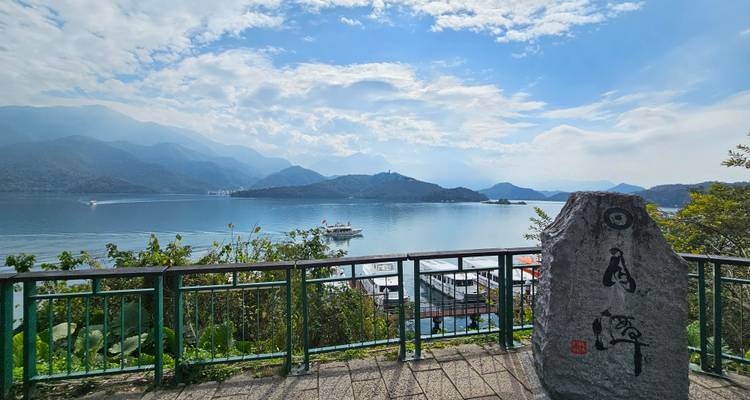 Terrasse d'observation surplombant le lac Sun Moon avec des garde-corps verts, des bateaux d'excursion et des montagnes bleues brumeuses.