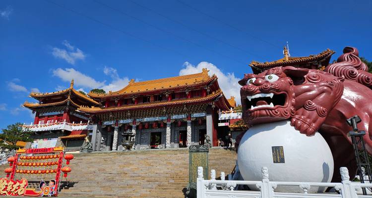 Temple Wenwu orné avec une statue de lion gardien rouge vif se détachant sur un ciel bleu éclatant.