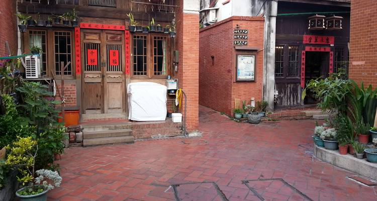 Cour tranquille en briques rouges avec des plantes en pot et des portes traditionnelles en bois ornées de distiques chinois.