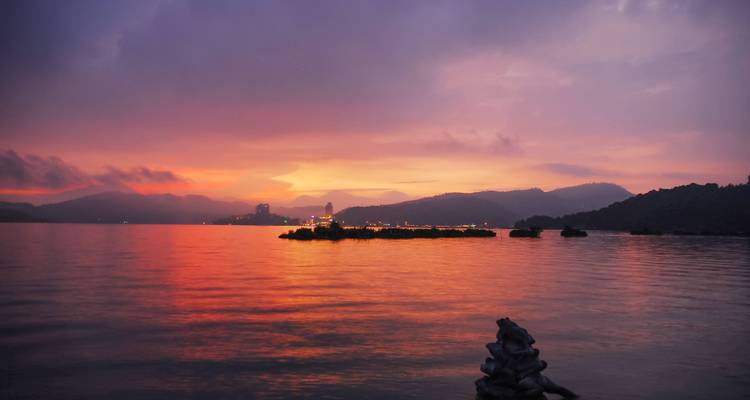 Coucher de soleil spectaculaire violet-orange sur le lac Sun Moon avec un ciel lumineux se reflétant sur l'eau calme.