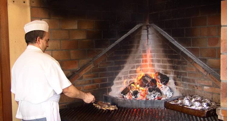 Chef cocinando carnes en una parrilla de llama abierta.