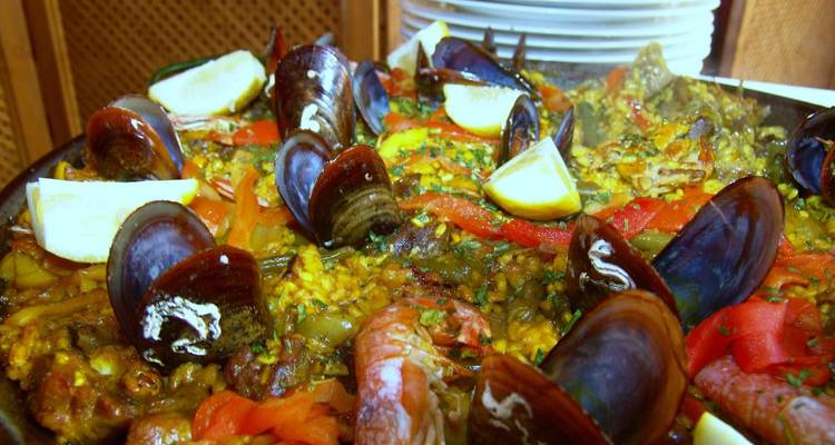 Primer plano de un plato de paella con mejillones, camarones y gajos de limón.