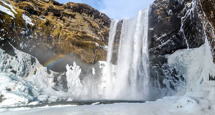 Frozen waterfall cascading down a rocky cliffside with a hint of rainbow.