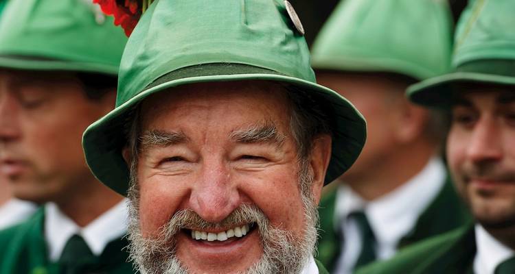 Smiling man in traditional Bavarian hat and green attire during a cultural festival.