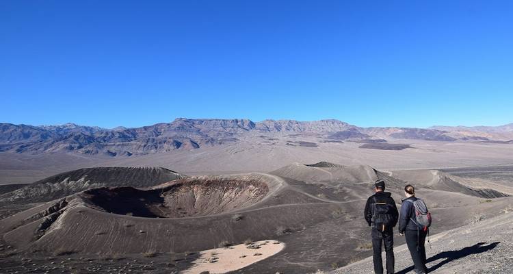Two hikers overlooking a volcanic crater in a desert landscape.