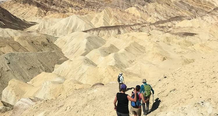 Hikers walking in a vast desert landscape with eroded hills.