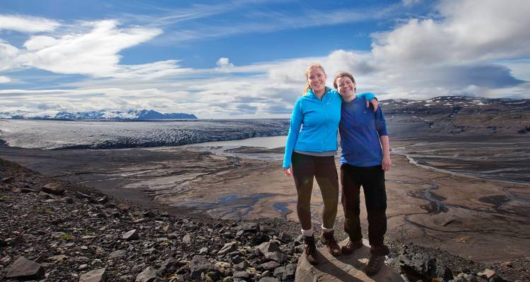 Zwei Menschen stehen auf einem Kamm mit Blick auf einen Gletscher und Berge.
