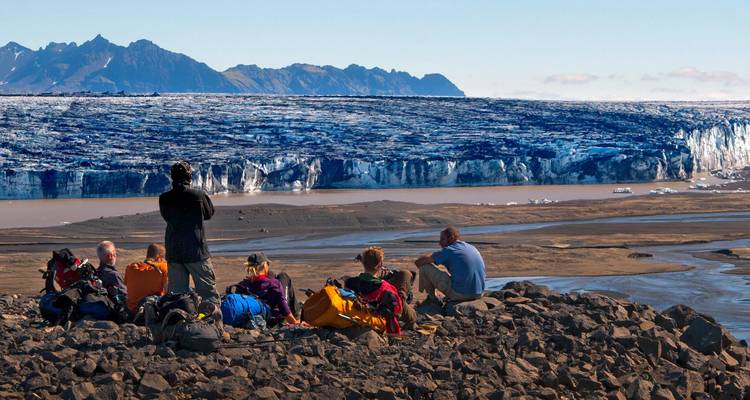 Gruppe sitzt mit Blick auf einen Gletscher und braune Landschaft.