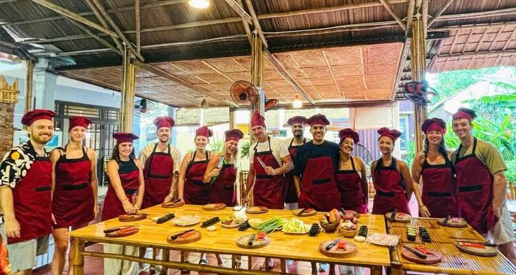 participantes de clase de cocina con delantales rojos posando alrededor de mesa de platos preparados