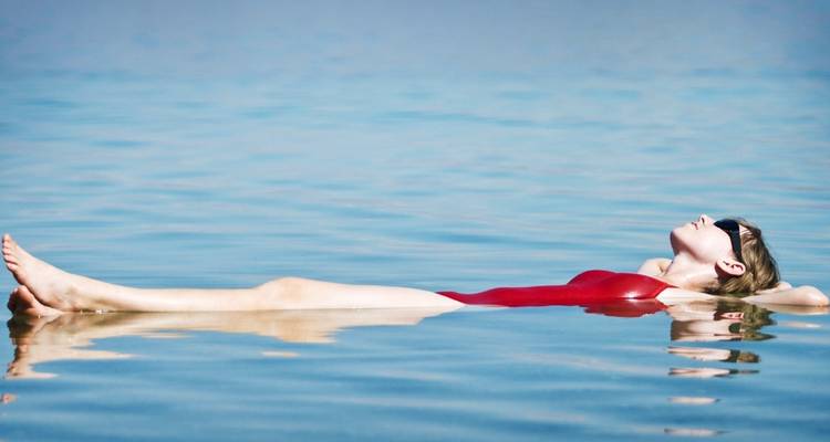 Een vrouw die moeiteloos drijft in de Dode Zee, gekleed in een rode badpak.