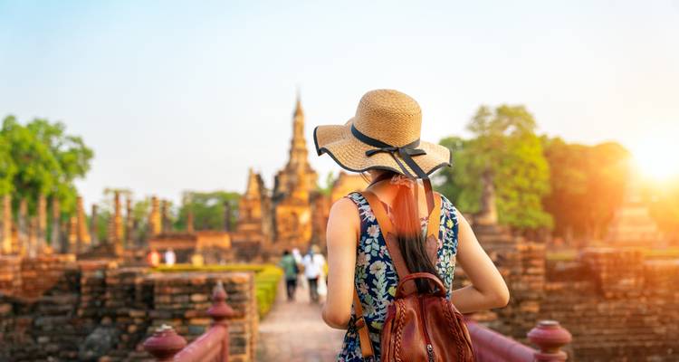 Mujer con sombrero mirando ruinas antiguas durante el atardecer.
