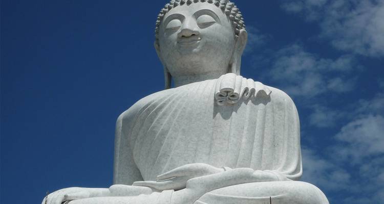 Une grande statue de Bouddha blanche sur fond de ciel bleu.