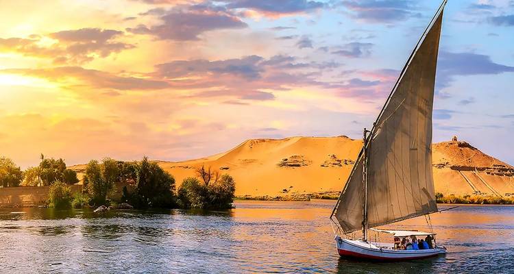 Traditional sailboat on a river during a vibrant sunset.
