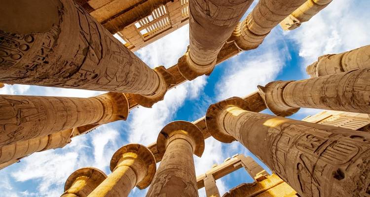 Ancient colonnade with hieroglyphs and clear blue sky.