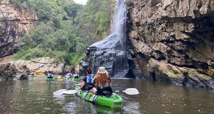 Des kayakistes pagaient dans une eau calme vers une cascade qui dévale, encadrée par des parois de canyon escarpées et de la verdure.