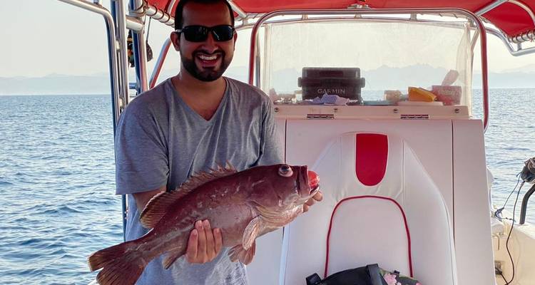 Mann hält einen großen Fisch auf einem Boot mit dem Meer im Hintergrund.