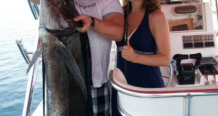 Zwei Personen posieren mit einem großen Fisch auf einem Boot.