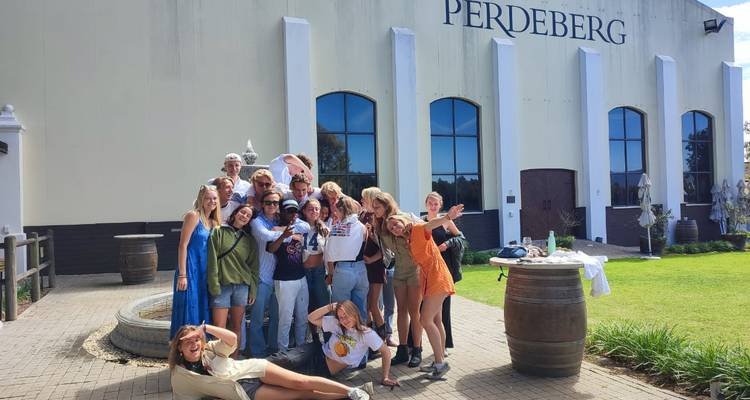 Un grand groupe touristique pose de manière ludique devant le bâtiment de la cave vinicole Perdeberg, célébrant ensemble sous le soleil.