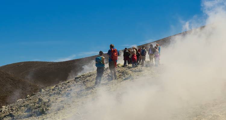 Groupe de touristes faisant de la randonnée sur une surface volcanique enfumée.