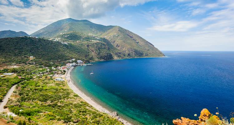 Vue panoramique d'une ville côtière avec un arrière-plan montagneux et une plage incurvée.