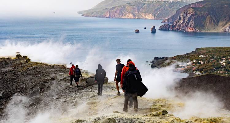 Groupe de personnes faisant de la randonnée près d'un paysage volcanique fumant avec la mer en arrière-plan.