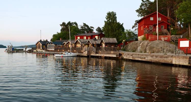 Malerische Bootshäuser aus Holz und rote Cottages säumen eine ruhige nordische Küstenlinie in der Abenddämmerung.