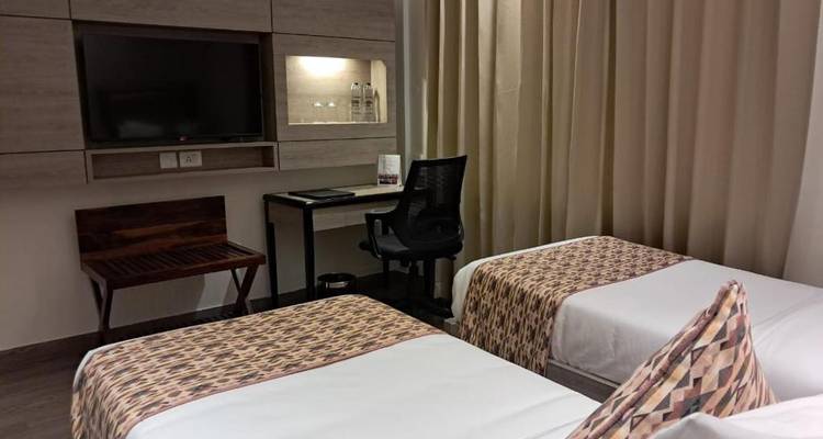 Habitación de hotel con dos camas individuales, escritorio y televisión.