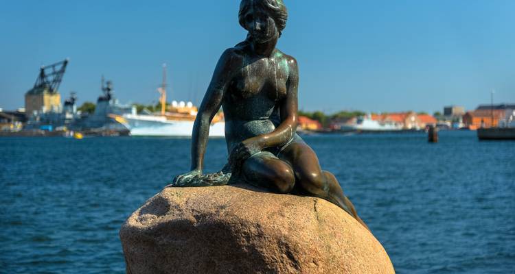 La statue de la Petite Sirène assise sur un rocher au bord de l'eau.