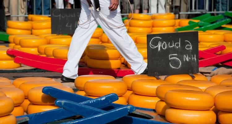 Des rangées de meules de Gouda orange vif empilées dans un marché traditionnel néerlandais de fromage.