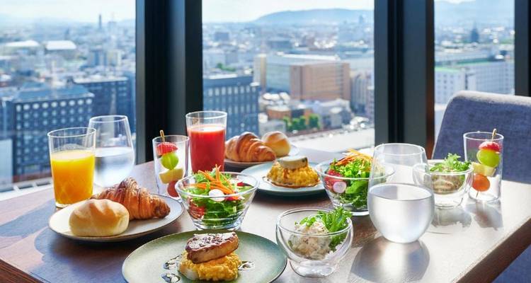 Table set with breakfast items and a panoramic city view through windows.
