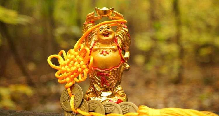 Golden laughing Buddha statue with a background of nature.