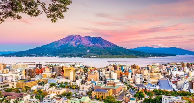 Cityscape with a volcano in the background during sunset.