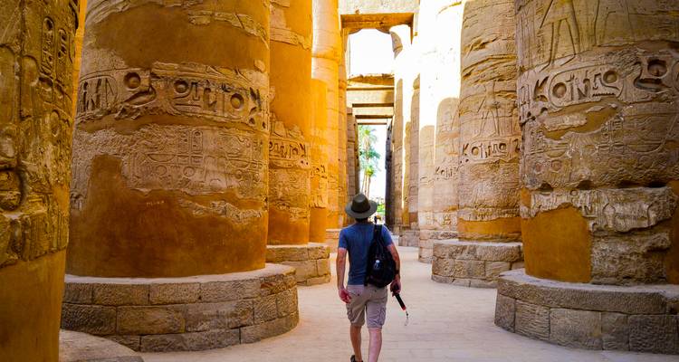 Person walking among ancient columns with hieroglyphs.