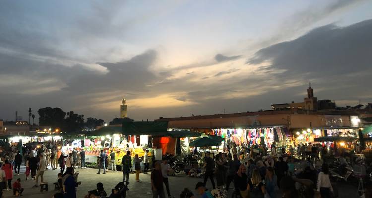Marché animé au crépuscule avec de nombreuses personnes et des étals de vendeurs.