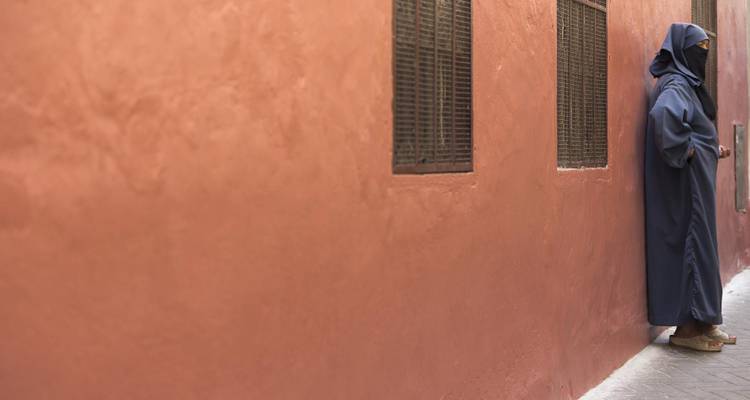 Person in traditional attire leaning against a wall.