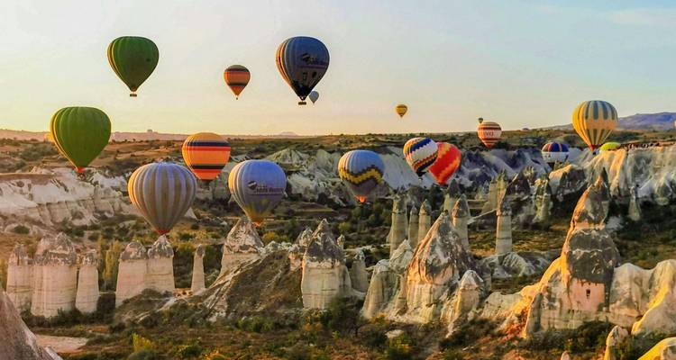 Numerous hot air balloons over a rocky landscape at sunrise.