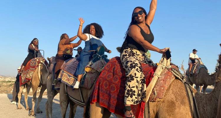 People riding camels against a desert backdrop.