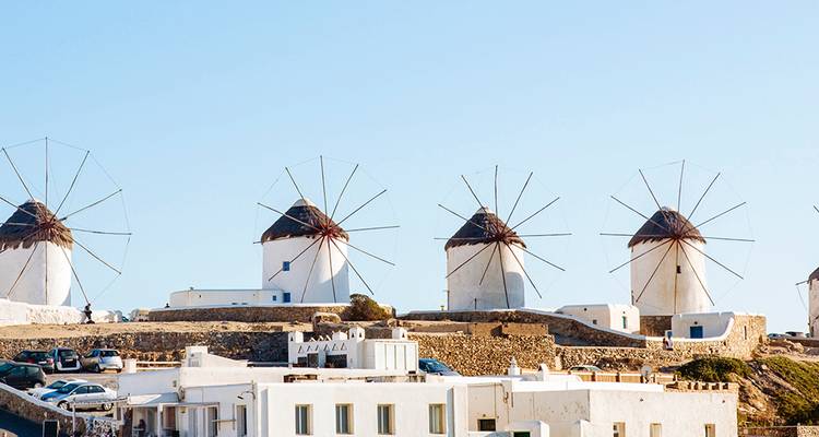 Ikonische weiße Windmühlen von Mykonos stehen auf einem Hügel über kubischen kykladischen Häusern vor einem klaren Himmel.