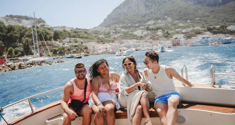 Quatre amis profitant d'une balade en hors-bord sur des eaux bleues scintillantes avec le littoral escarpé et la ville blanchie à la chaux de Capri qui s'élève derrière.