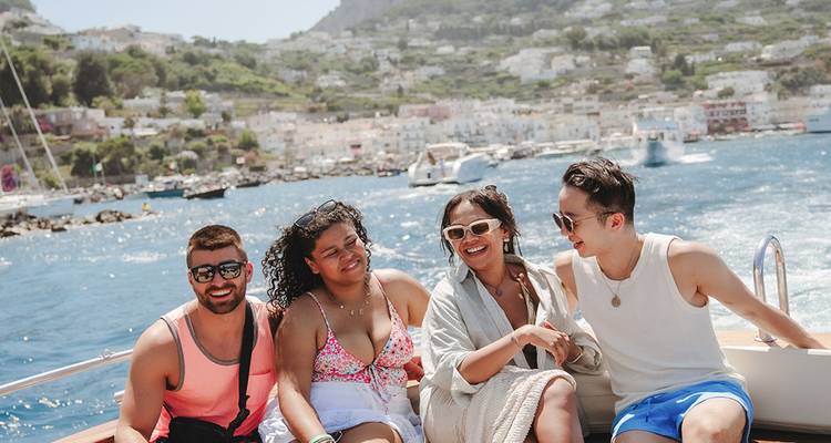 Groep vrienden geniet van een speedbootrit voor de kust van Capri met een stad op de heuvel op de achtergrond.