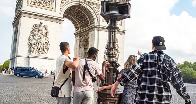 Travellers point up at Paris’s Arc de Triomphe while discussing its historic reliefs.