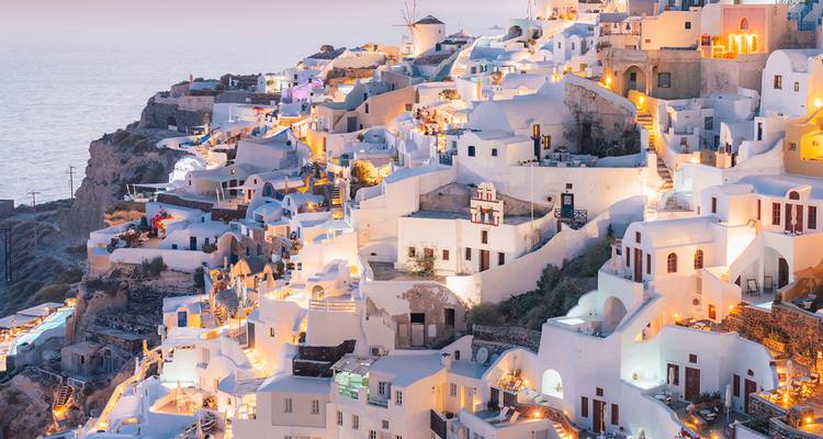 Icónicas casas encaladas en el acantilado de Oia brillando con luces al atardecer con vista al Mar Egeo