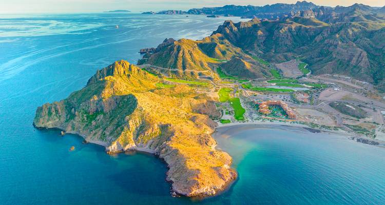 Luchtfoto van een kustlandschap met bergen en helder blauw water.
