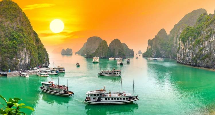 Le coucher de soleil doré illumine les eaux émeraude parsemées de bateaux touristiques et de formations karstiques imposantes.